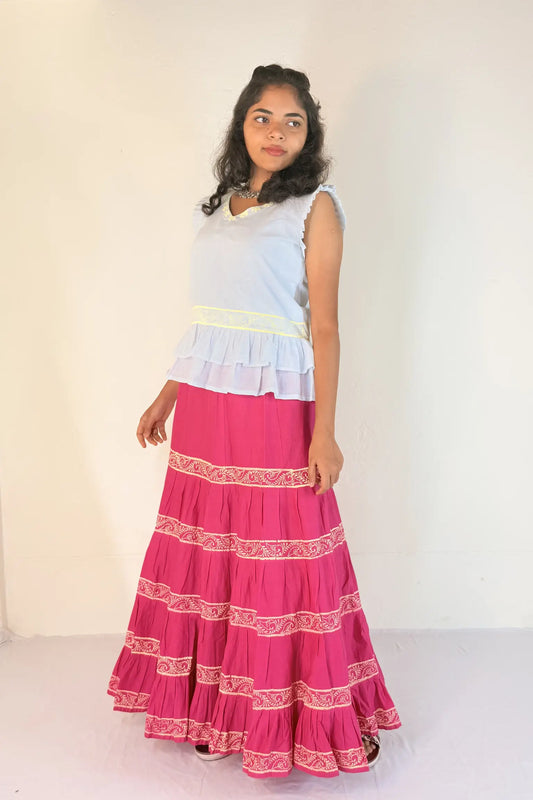 Woman wearing a white top and pink skirt with white patterns on a white background