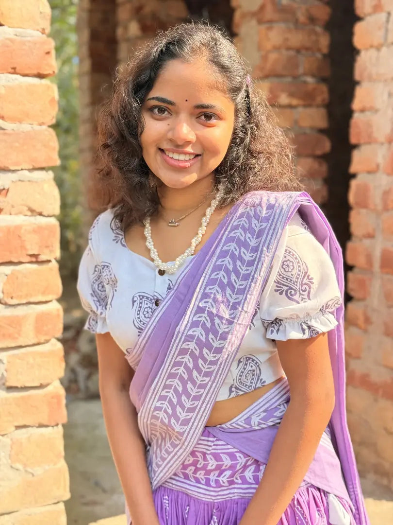 A woman wearing a purple and white Gopi Skirt Set is standing in front of a brick wall.