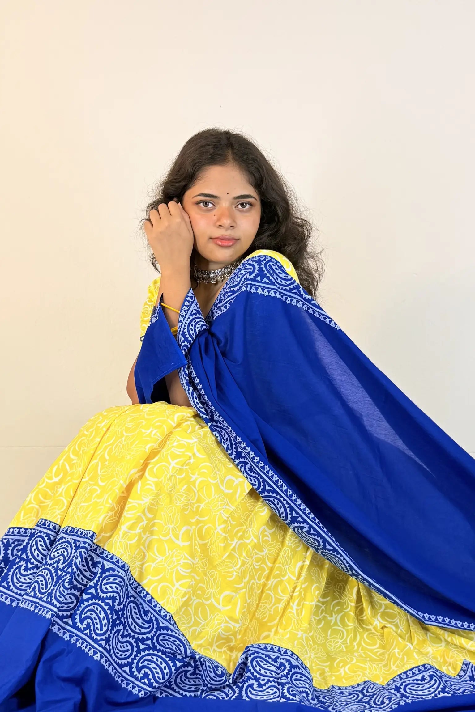 Woman wearing a yellow and blue traditional outfit with a plain background
