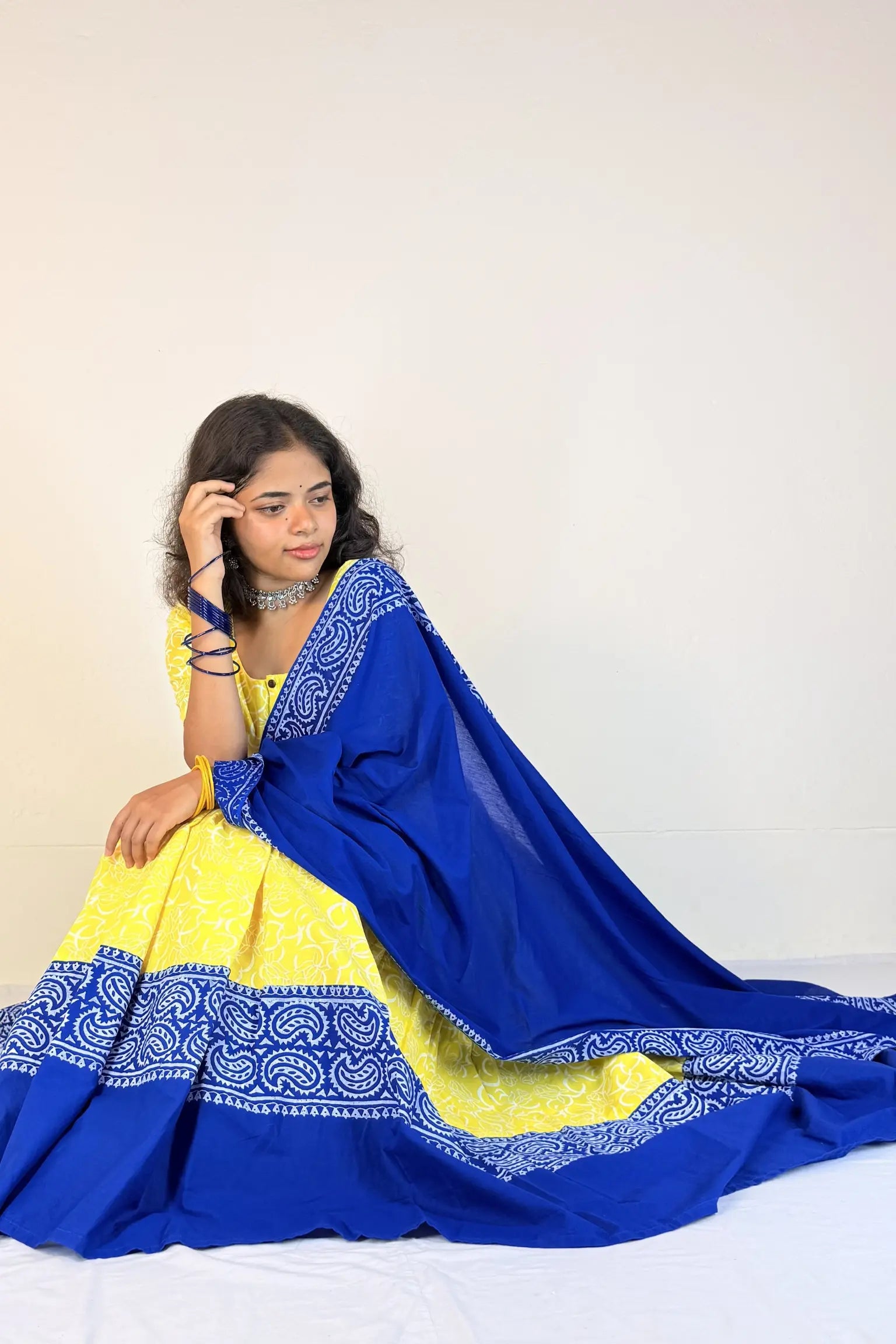 Woman wearing a blue and yellow traditional outfit with intricate patterns on a white background