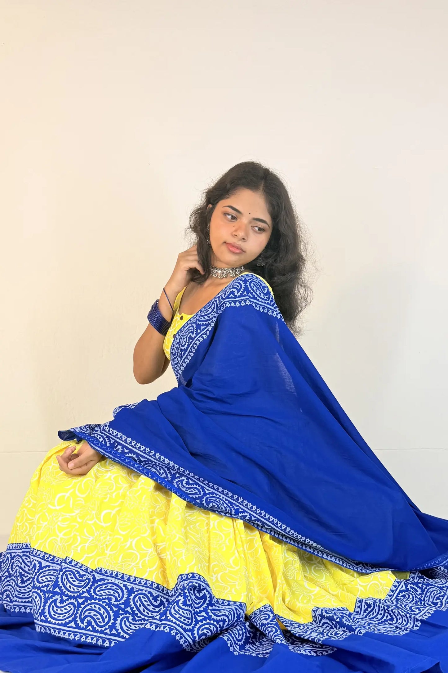 Woman wearing a blue and yellow traditional outfit with a plain background