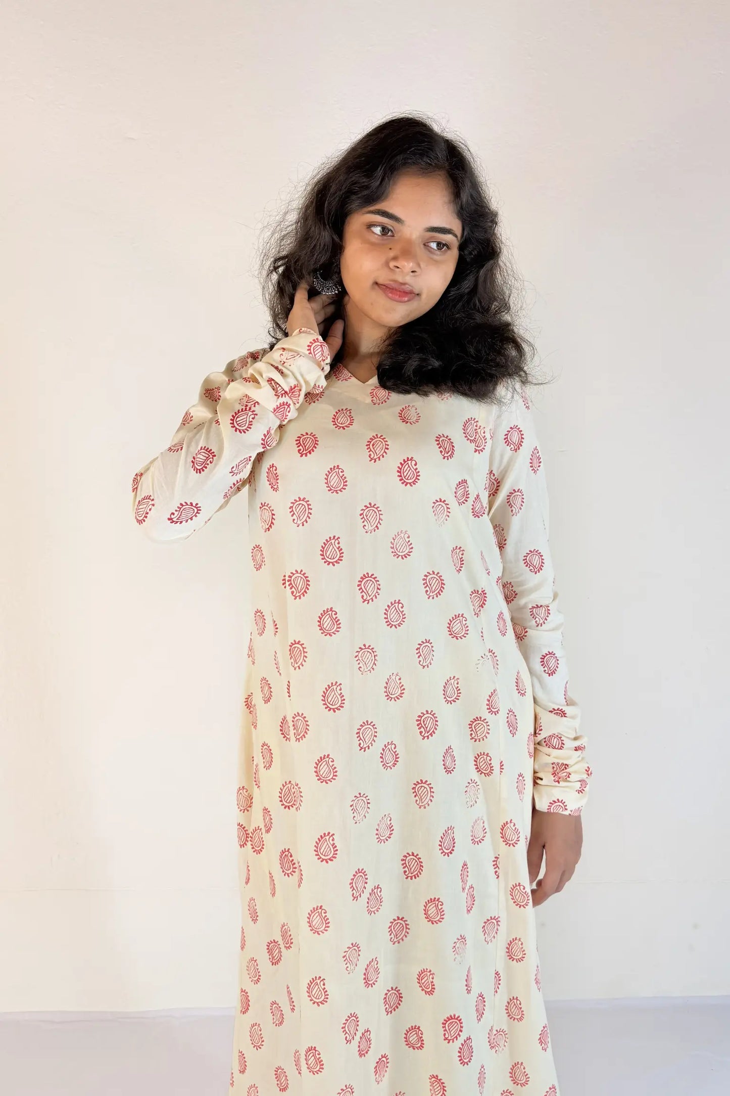 Woman wearing a long, light-colored dress with pink floral pattern against a plain background