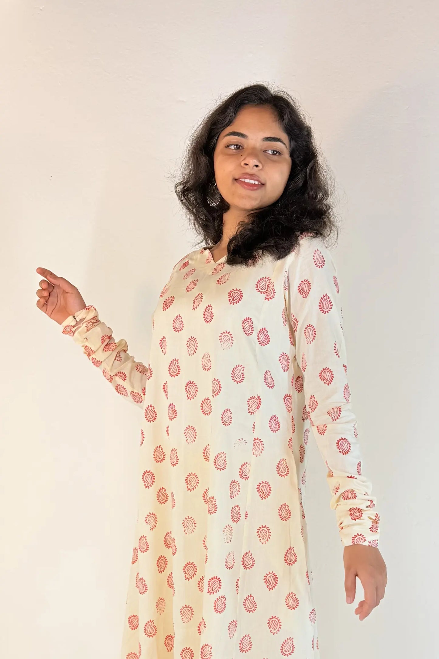 Woman wearing a long, light-colored dress with pink floral pattern against a plain background