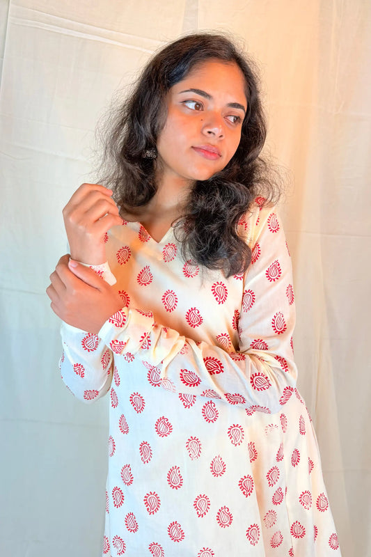 Woman wearing a white dress with red floral patterns against a neutral background