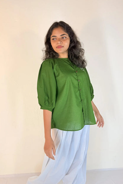 Woman wearing a green blouse and light blue pants against a plain background
