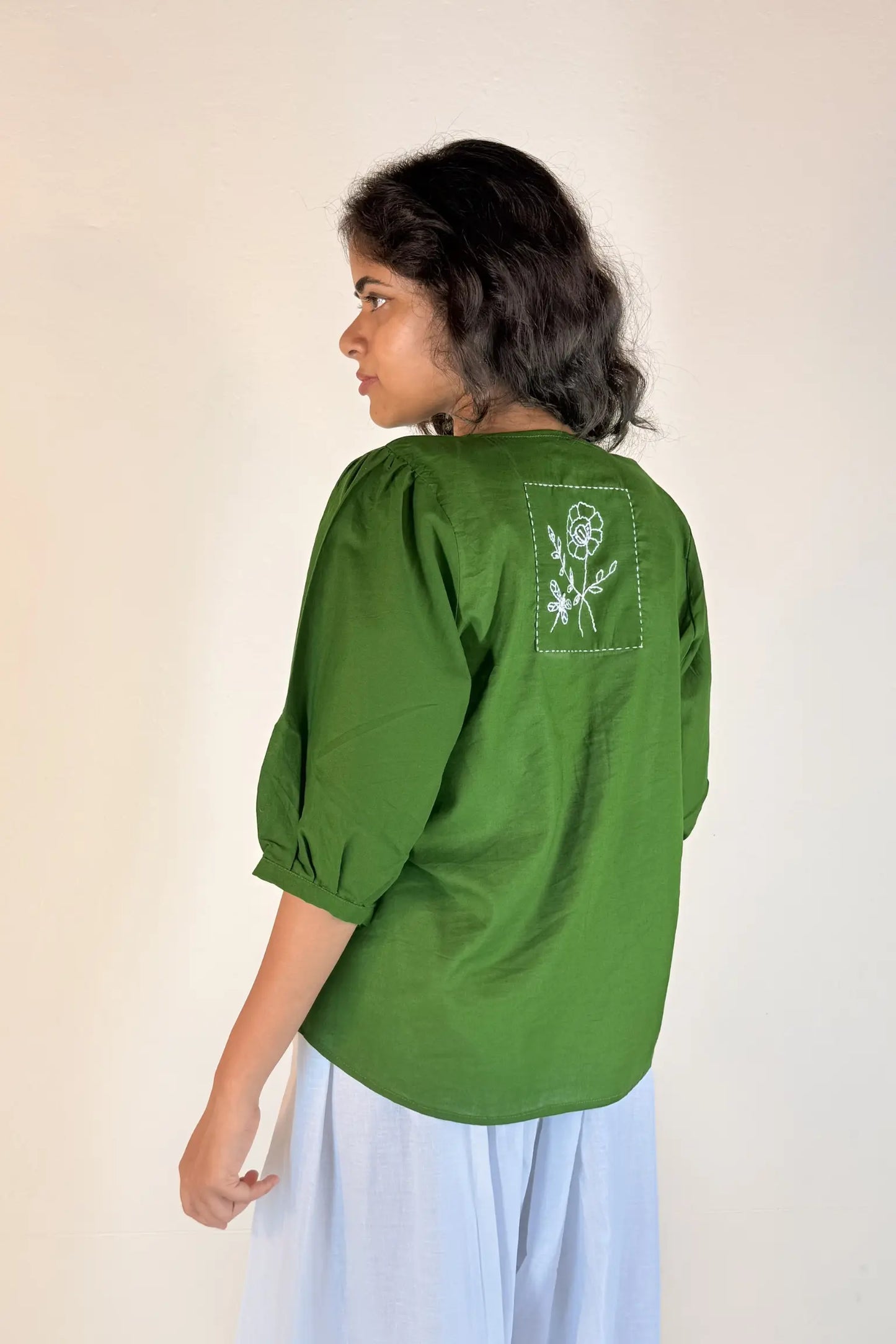 Woman wearing a green blouse with a floral design on the back against a plain background