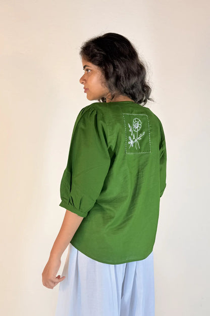 Woman wearing a green blouse with a floral design on the back against a plain background