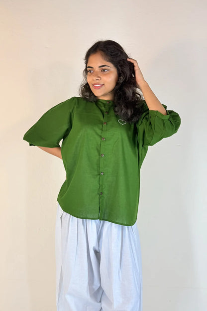 Woman wearing a green blouse and white pants against a plain background