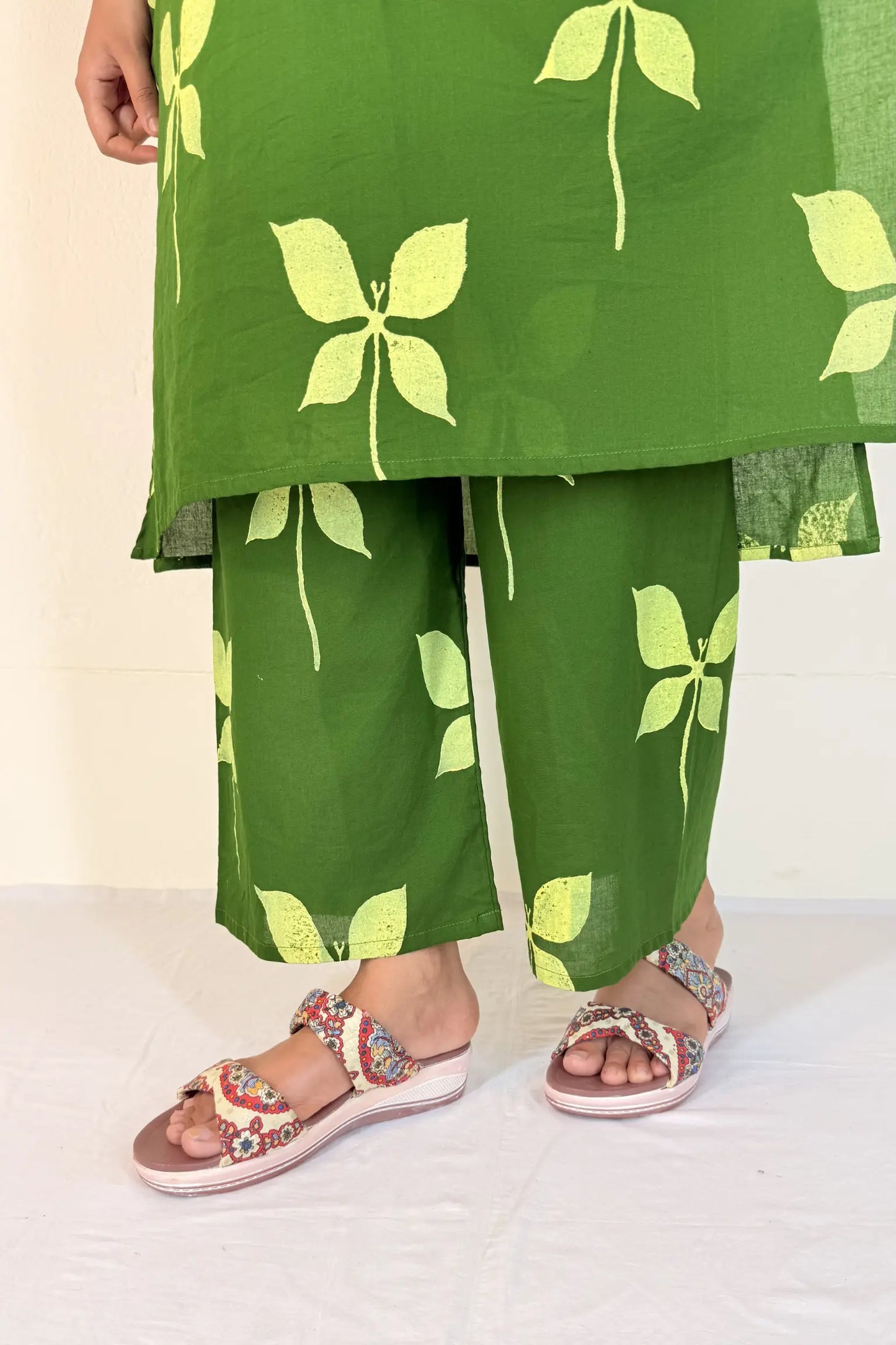 Green outfit with leaf patterns and sandals on a white background