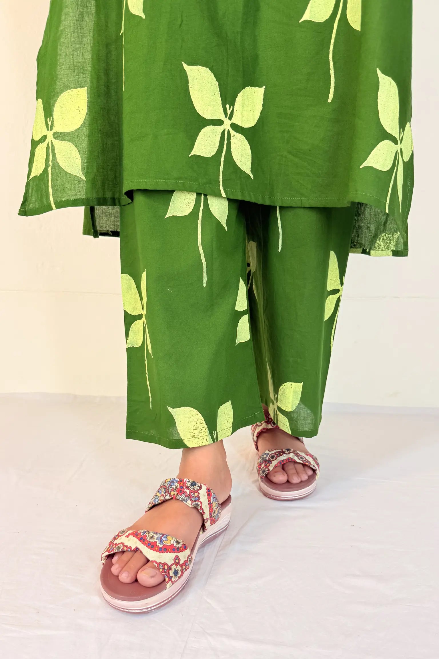 Green leaf-patterned outfit with floral sandals on a white background