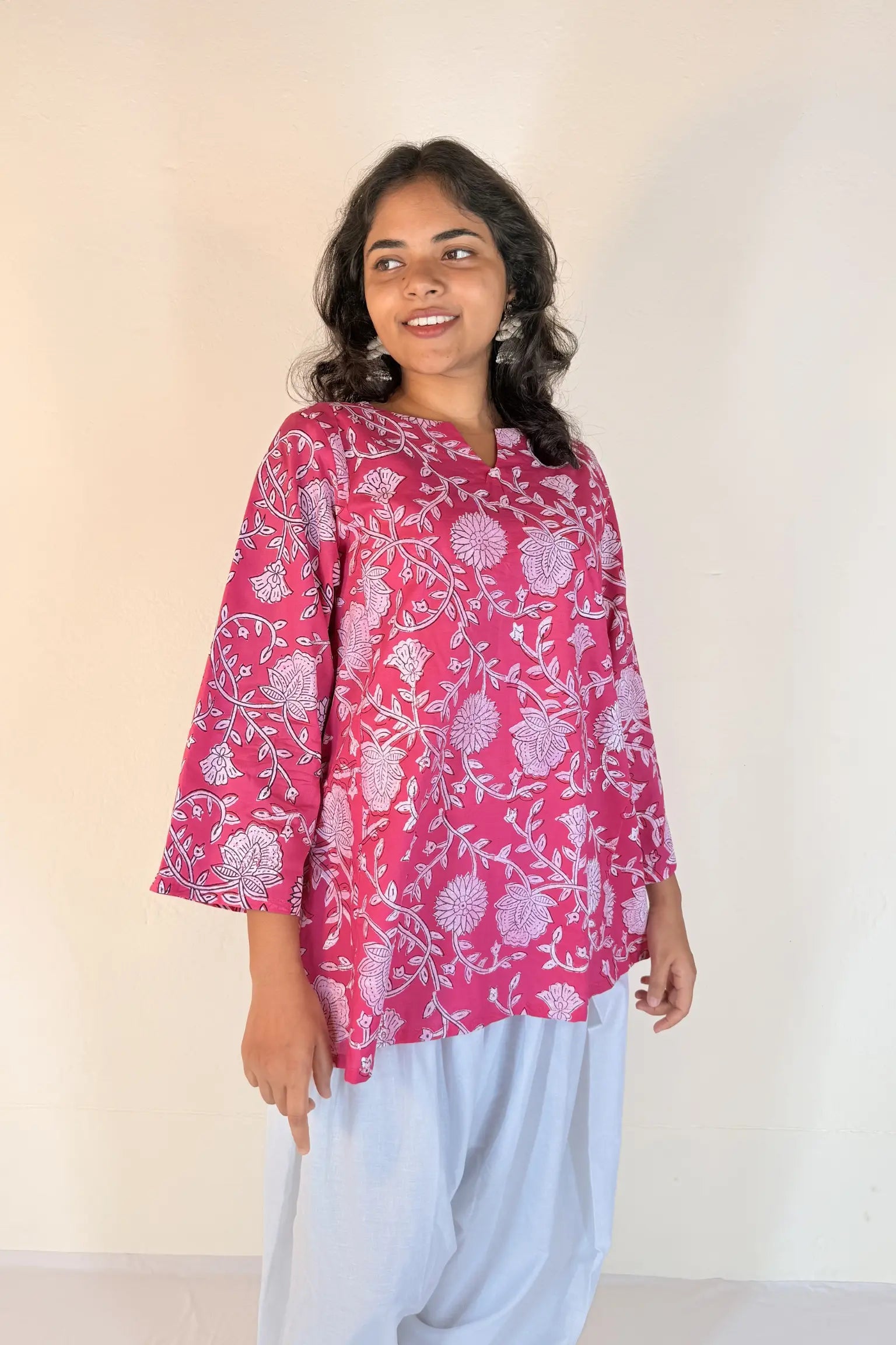 Woman wearing a pink floral blouse with white pants against a plain background