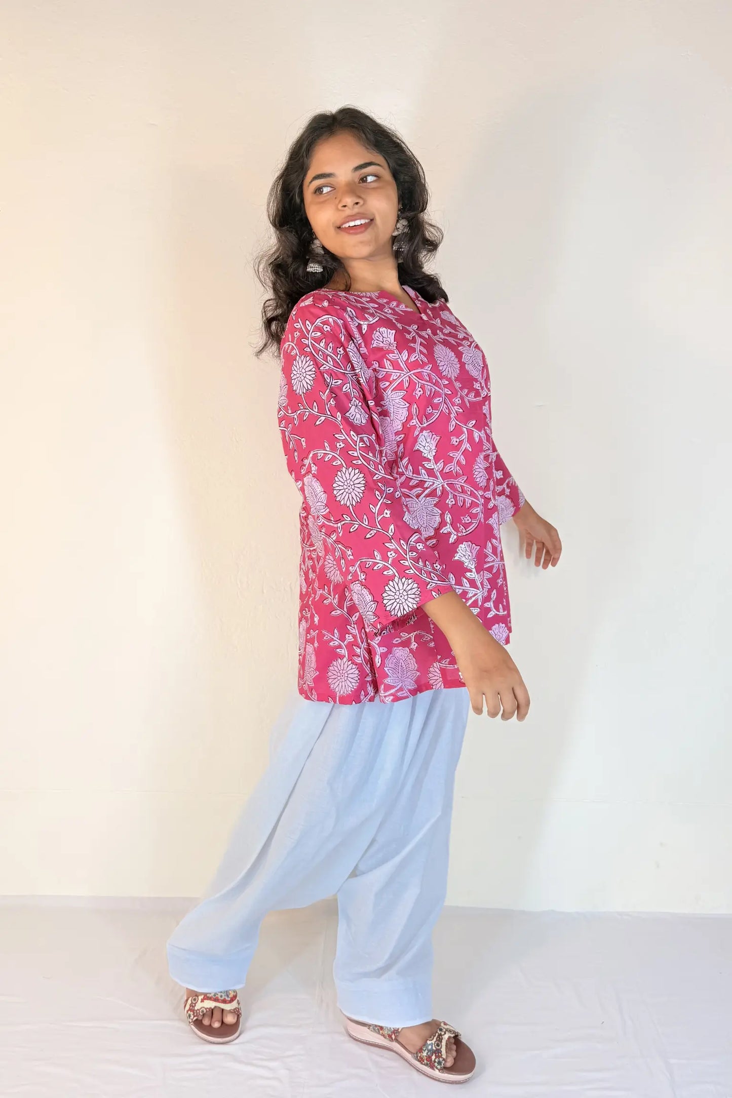 Woman wearing a pink floral top and light blue pants against a white background