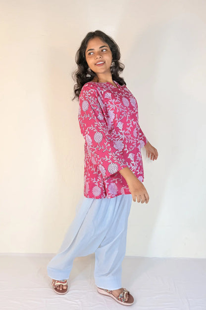 Woman wearing a pink floral top and light blue pants against a white background