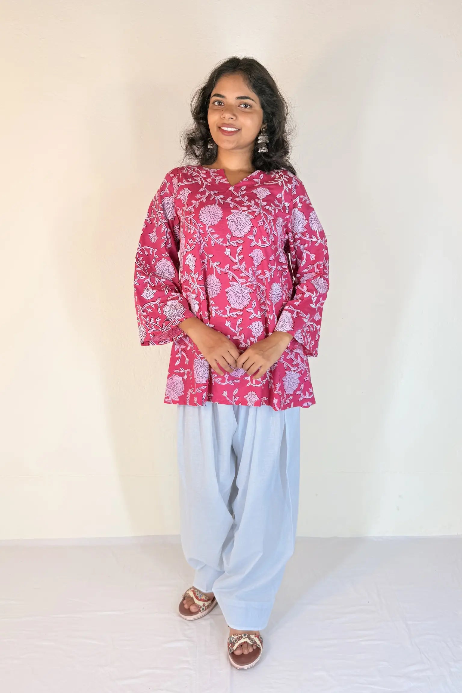 Woman wearing a pink floral top and light blue pants against a white background