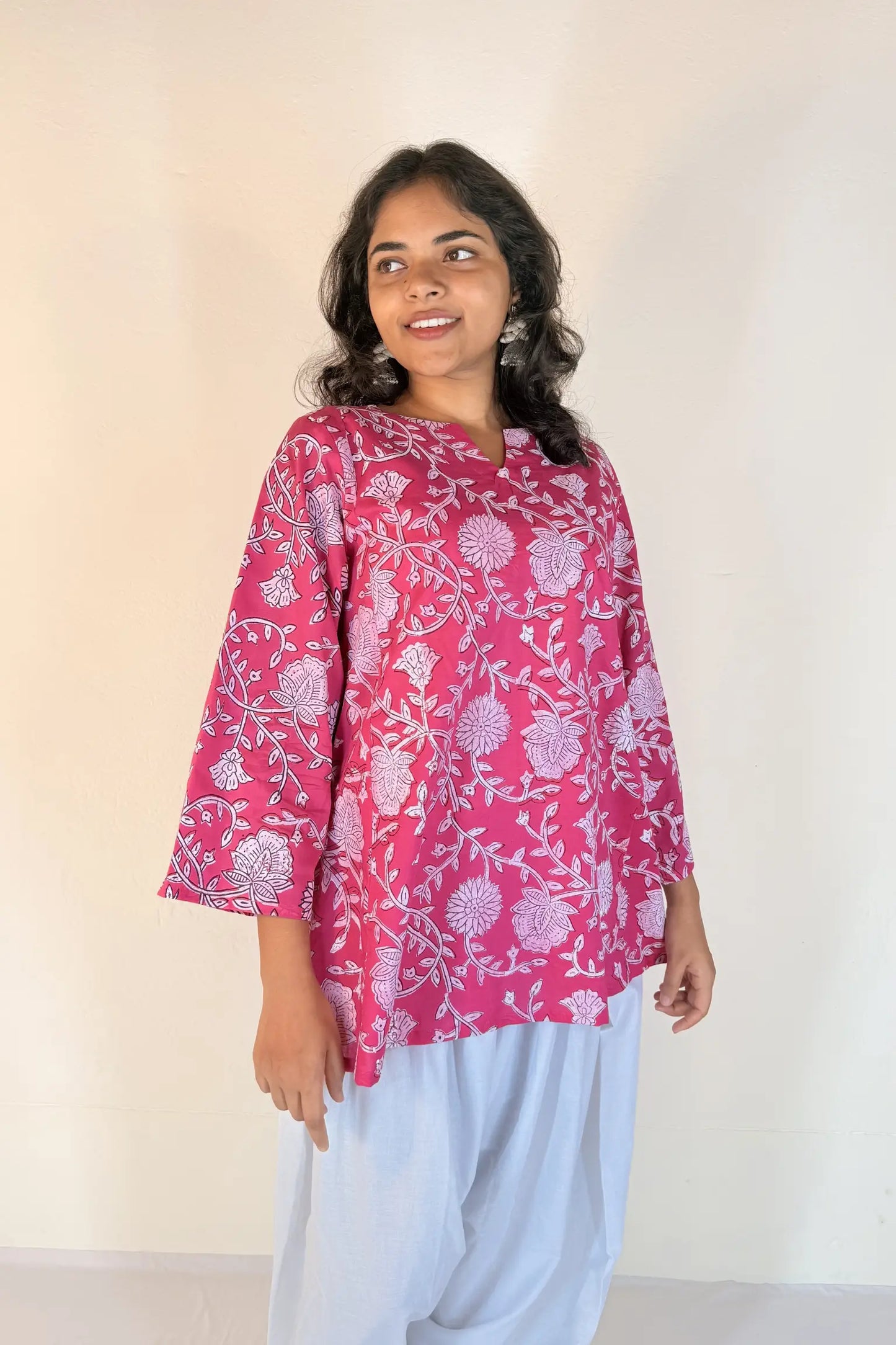 Woman wearing a pink floral blouse and light blue pants against a white background
