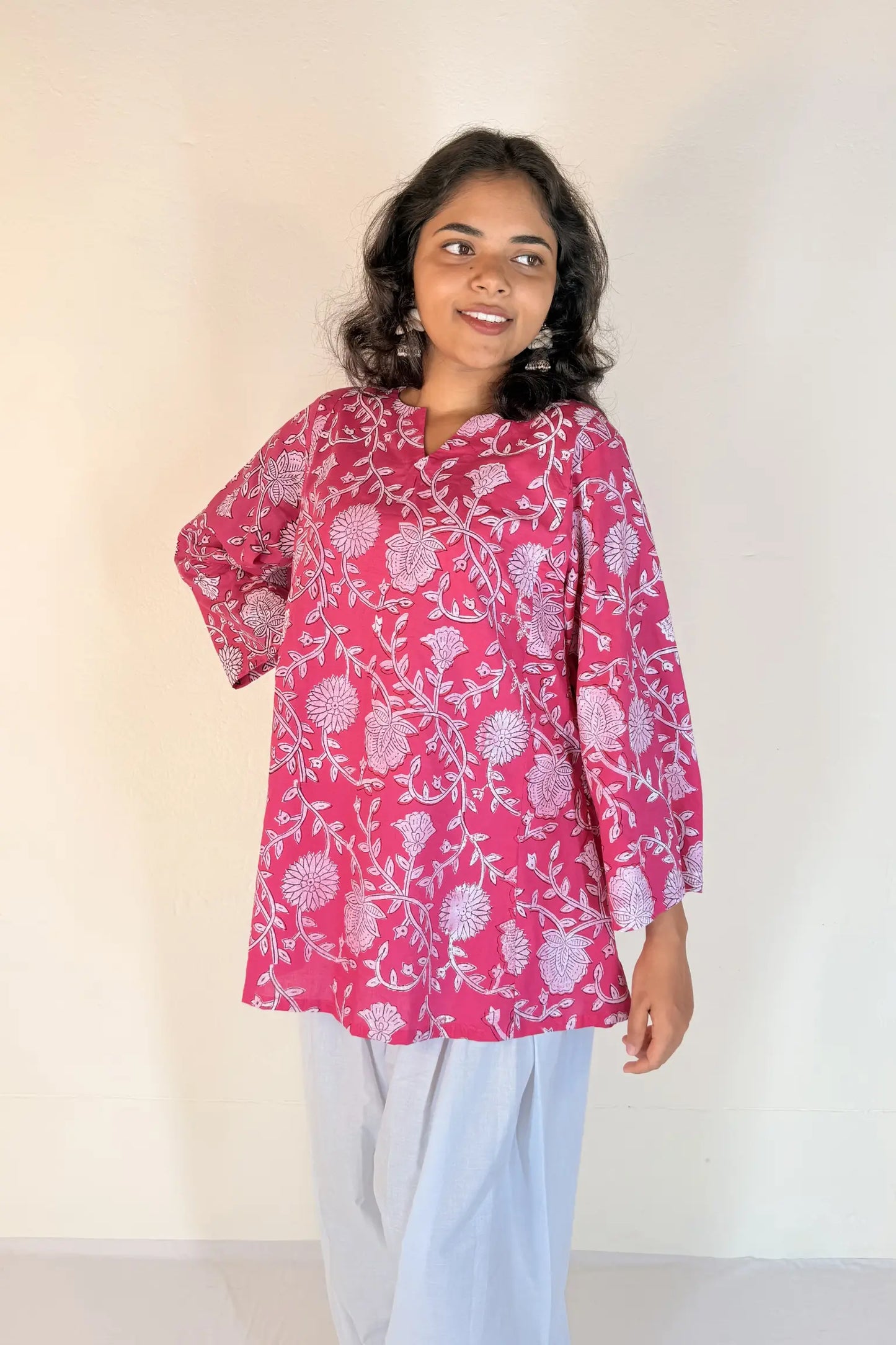 Woman wearing a pink floral blouse with white pants against a plain background