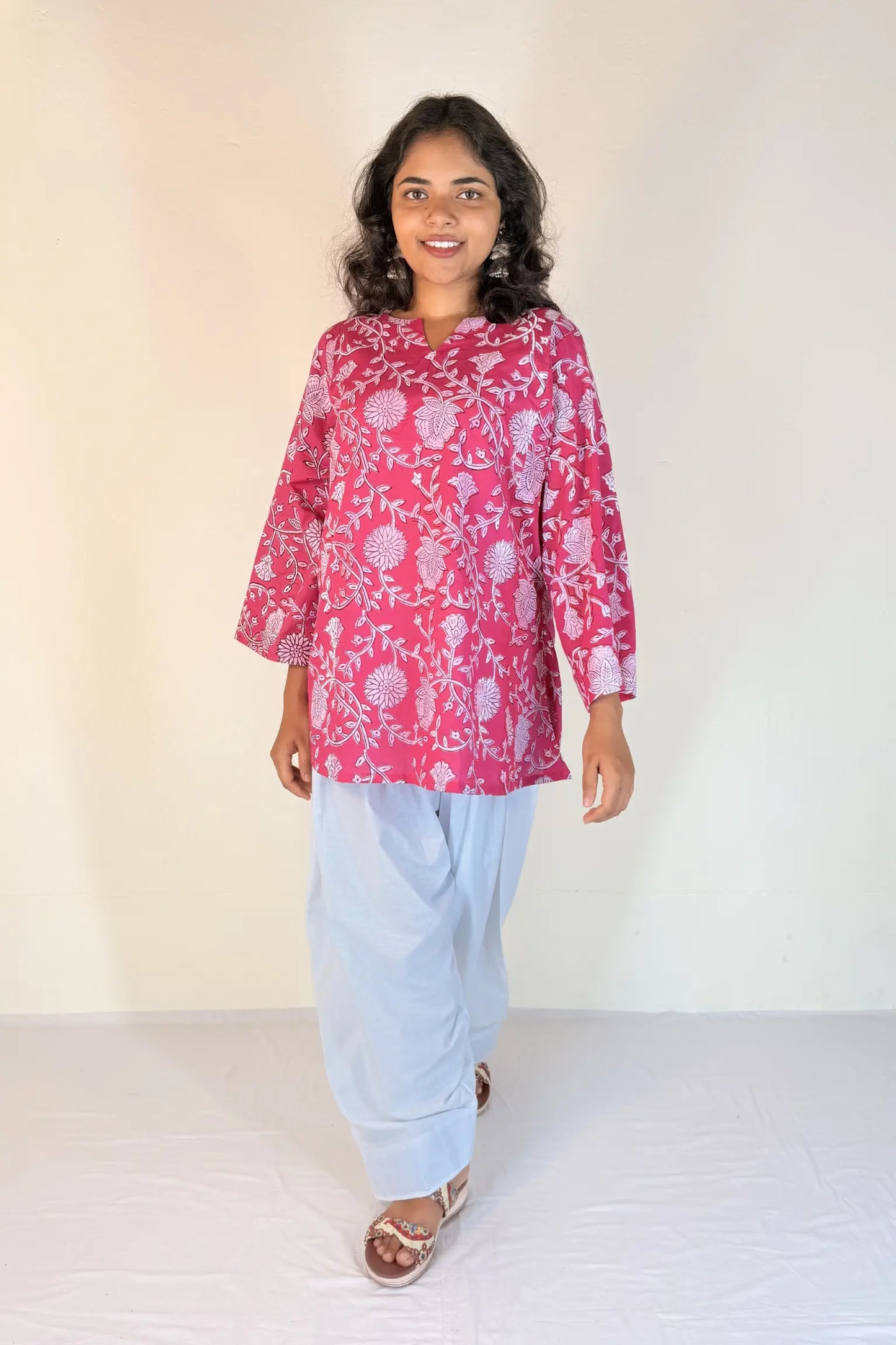 Woman wearing a pink floral top and light blue pants against a white background