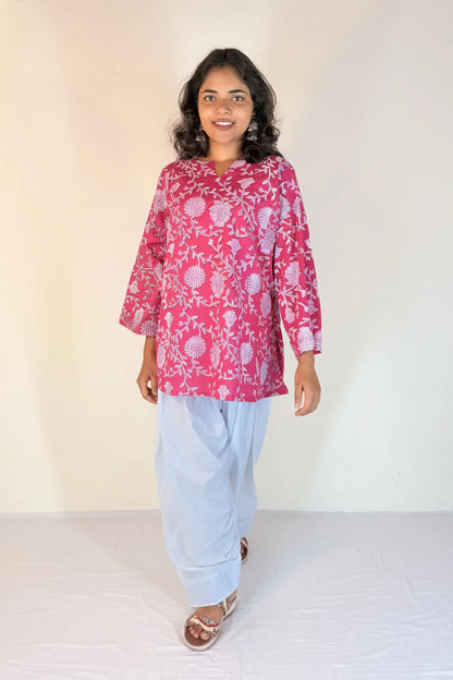 Woman wearing a pink floral top and light blue pants against a white background