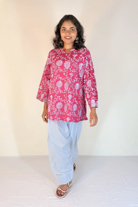 Woman wearing a pink floral top and light blue pants against a white background