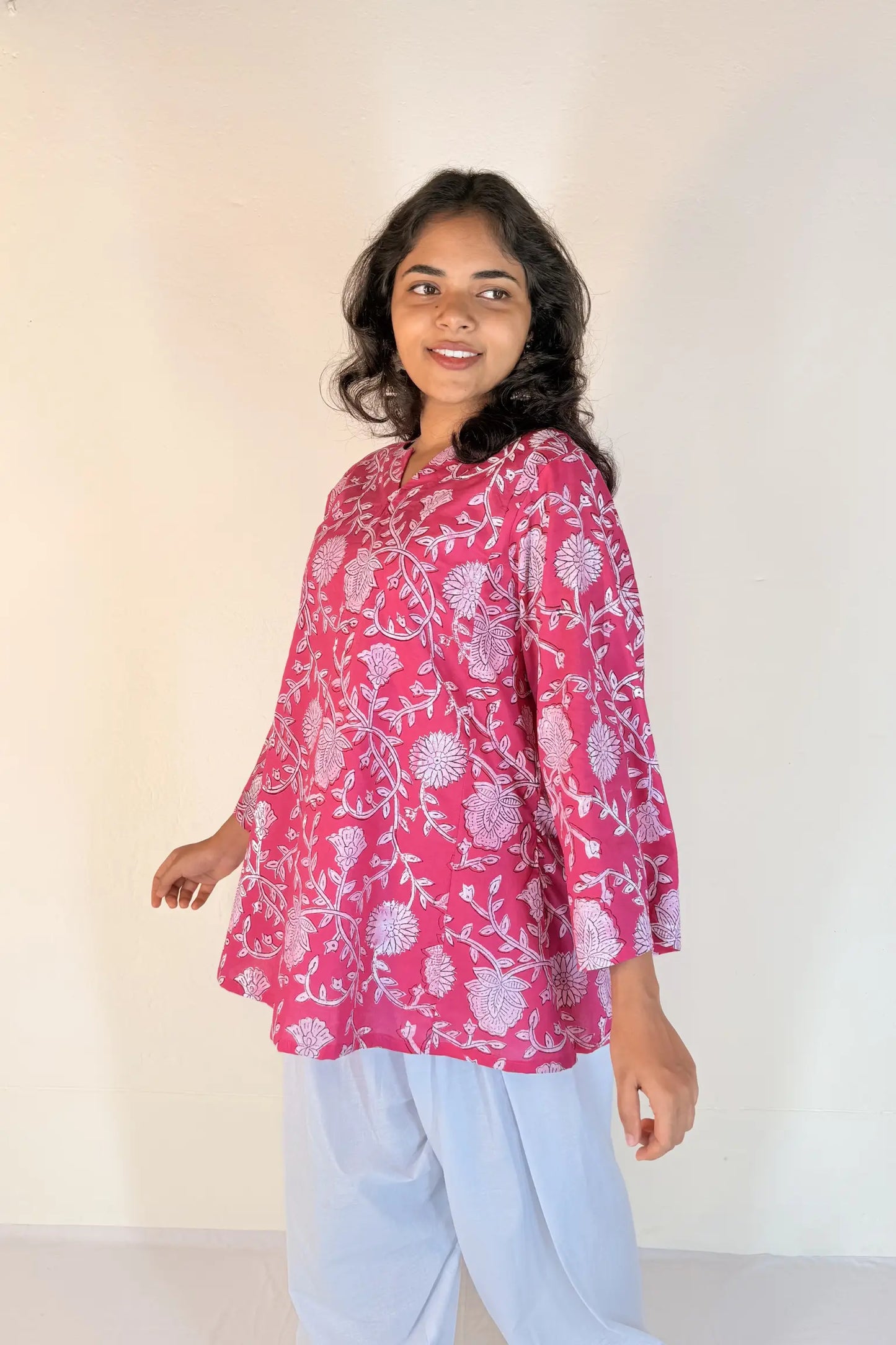Woman wearing a pink floral top and light blue pants against a white background