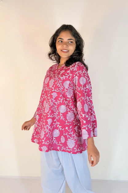 Woman wearing a pink floral top and light blue pants against a white background