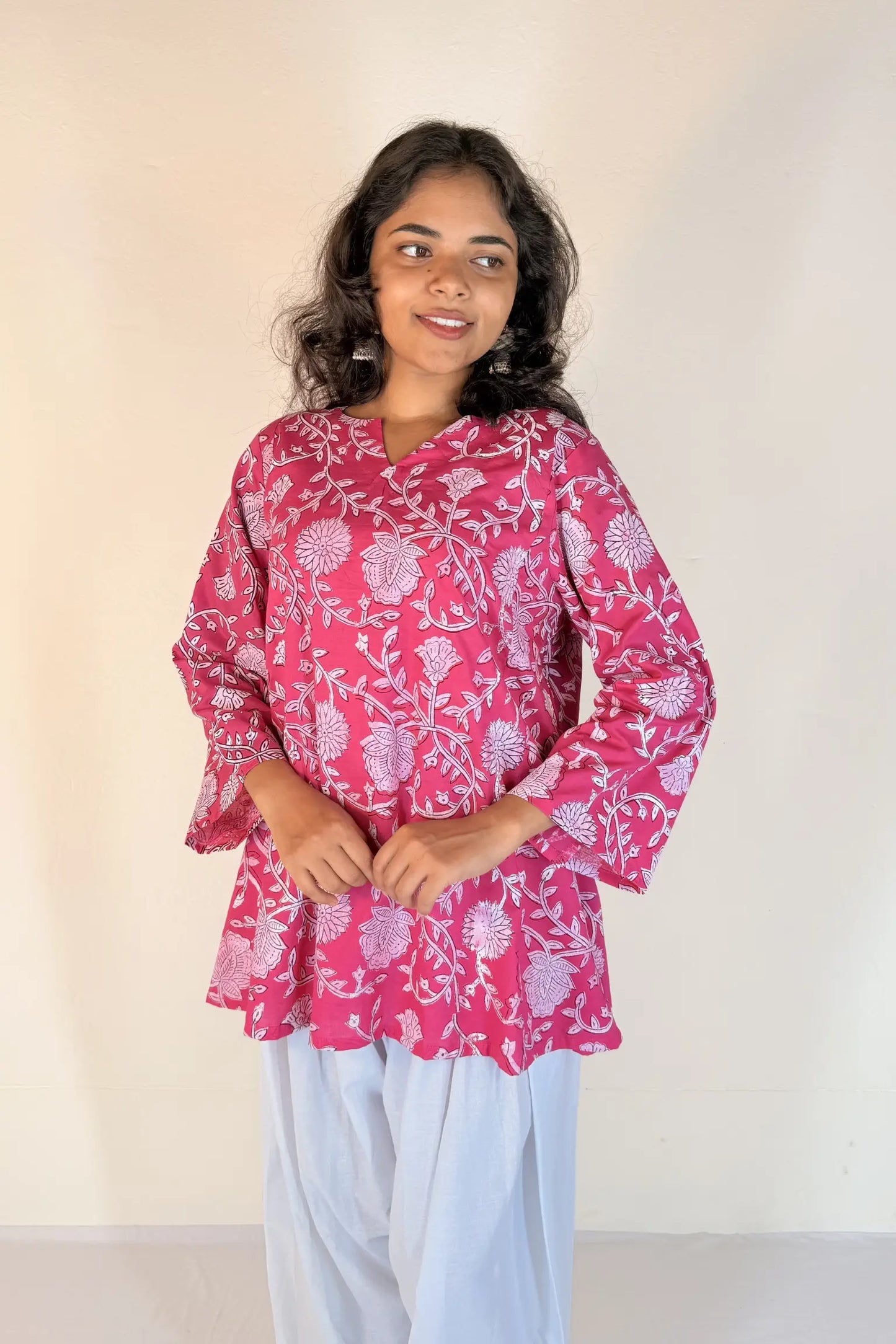 Woman wearing a pink floral blouse with white pants against a plain background