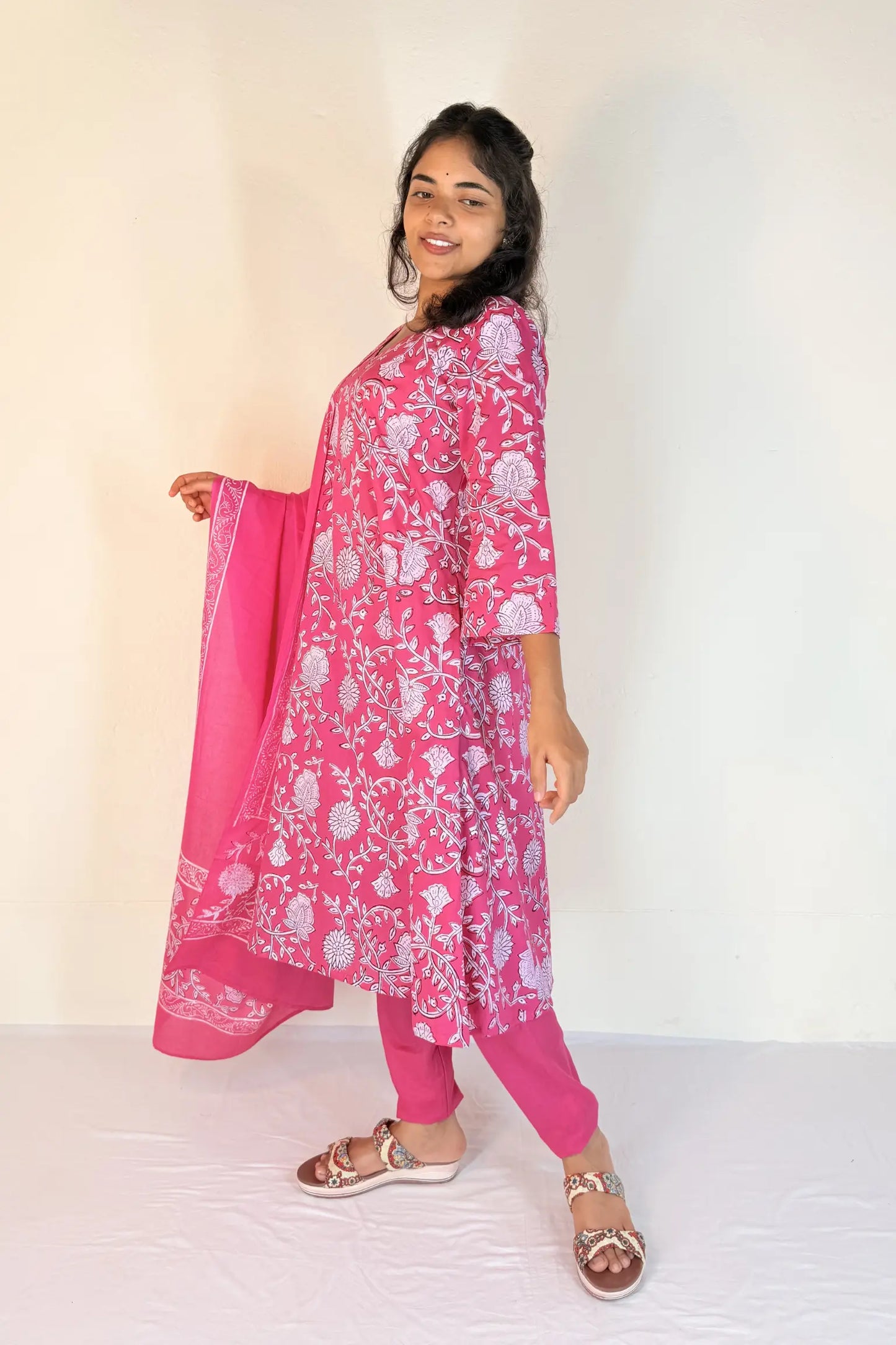 Woman wearing a pink traditional outfit with a white floral pattern on a plain background
