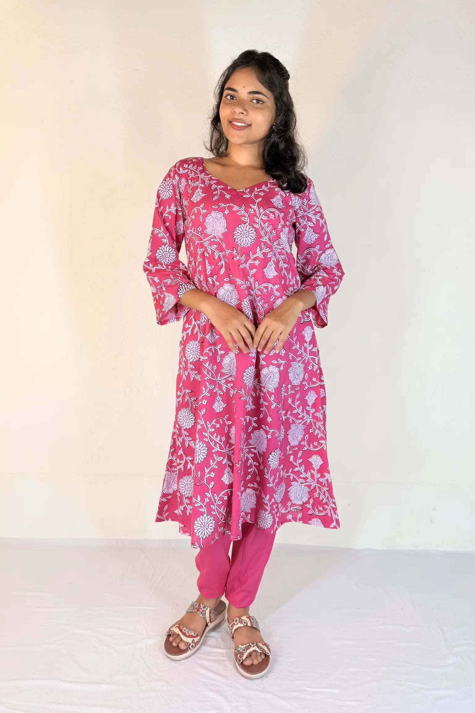 Woman wearing a pink floral kurta with matching pants against a white background