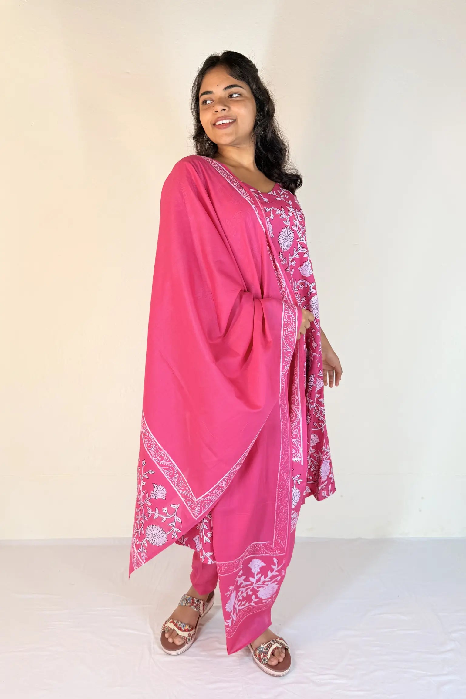 Woman wearing a pink traditional outfit with white patterns on a plain background