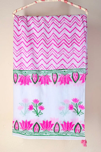 A white fabric wall hanging or towel with a pink and green printed pattern, suspended from a woven cord against a plain beige wall.