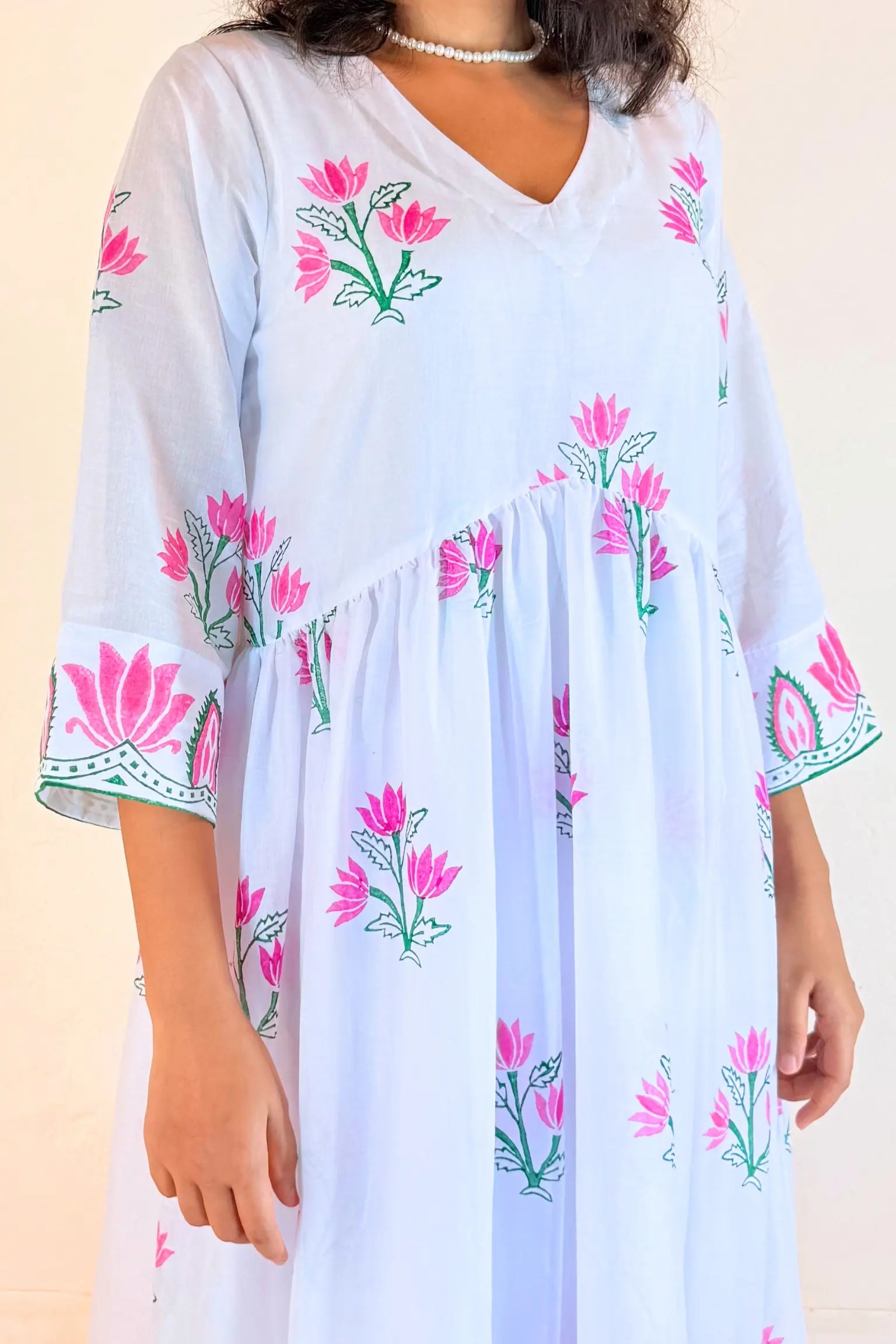 A woman wearing a light blue kaftan dress with pink and green floral block prints and embroidered details on the sleeves, set against a plain beige background.