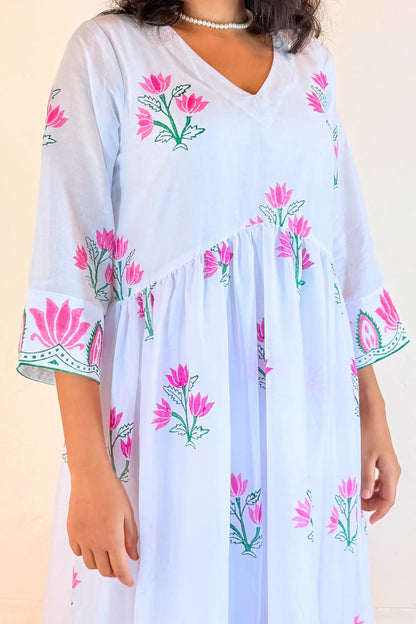 A woman wearing a light blue kaftan dress with pink and green floral block prints and embroidered details on the sleeves, set against a plain beige background.