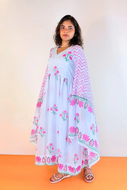 A woman modeling a light blue, long-sleeved, V-neck kurta with pink floral prints and a pink chevron-patterned dupatta, standing against a plain beige wall and orange floor.
