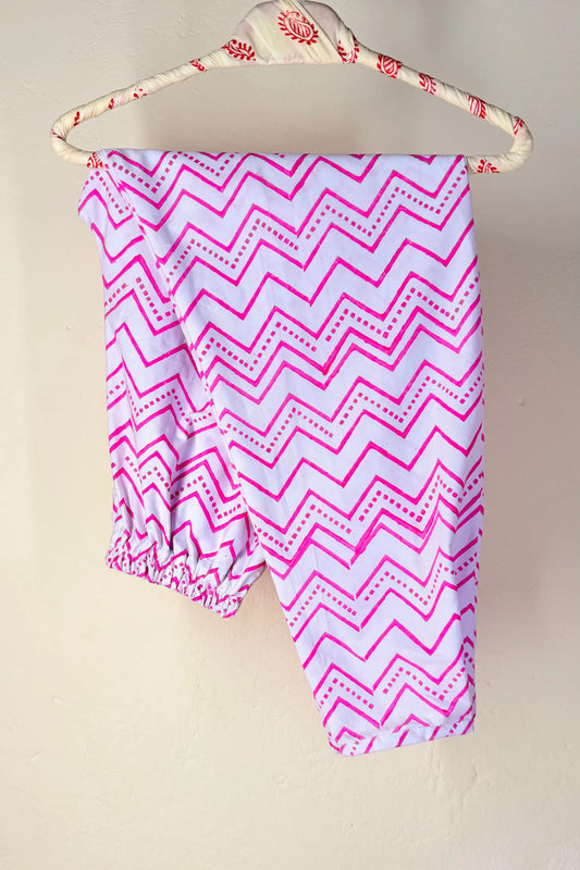 Pink and white chevron patterned baby leggings hanging on a decorative hanger against a plain beige wall.