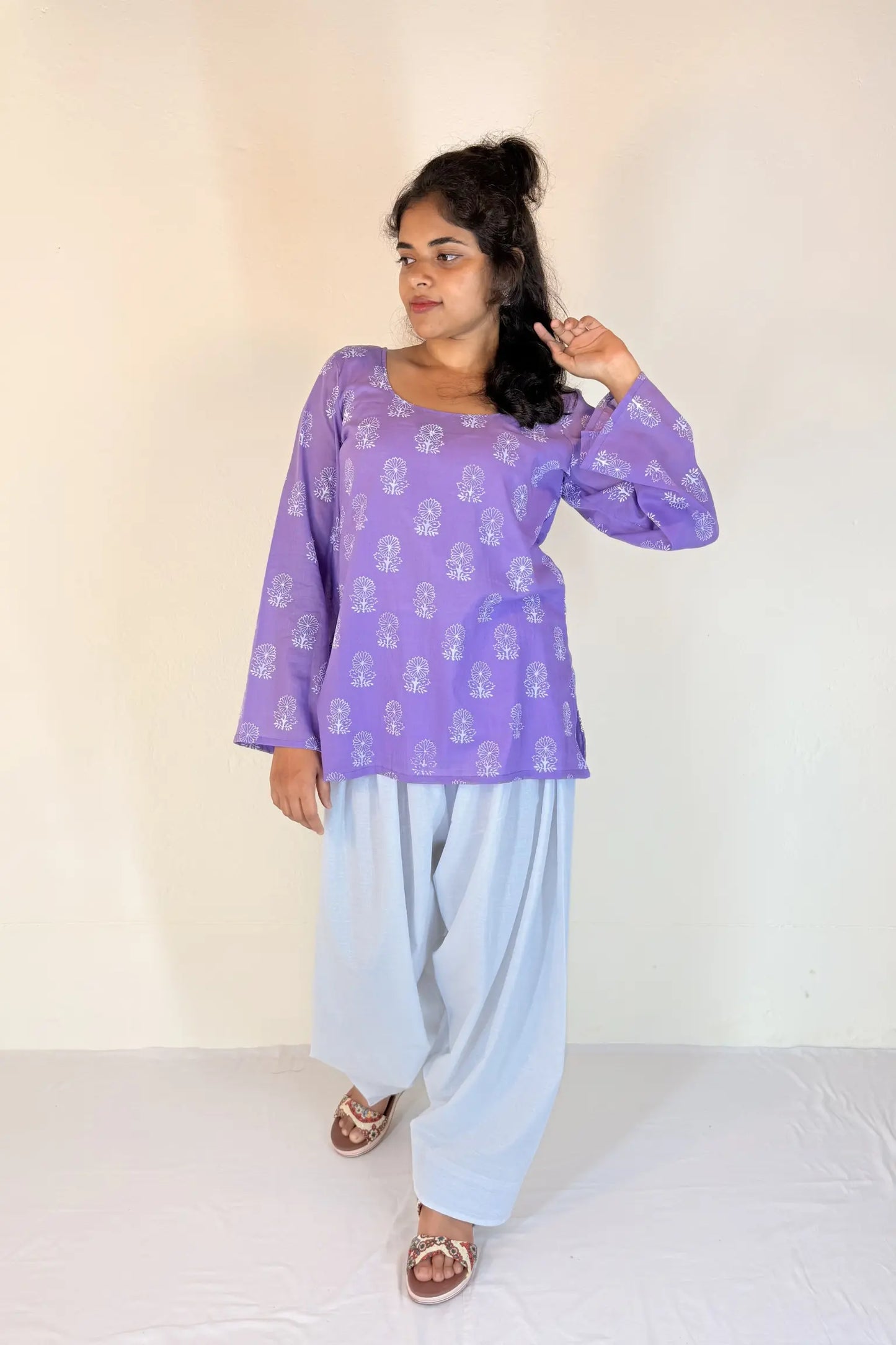 Woman wearing a purple top and light blue pants on a white background