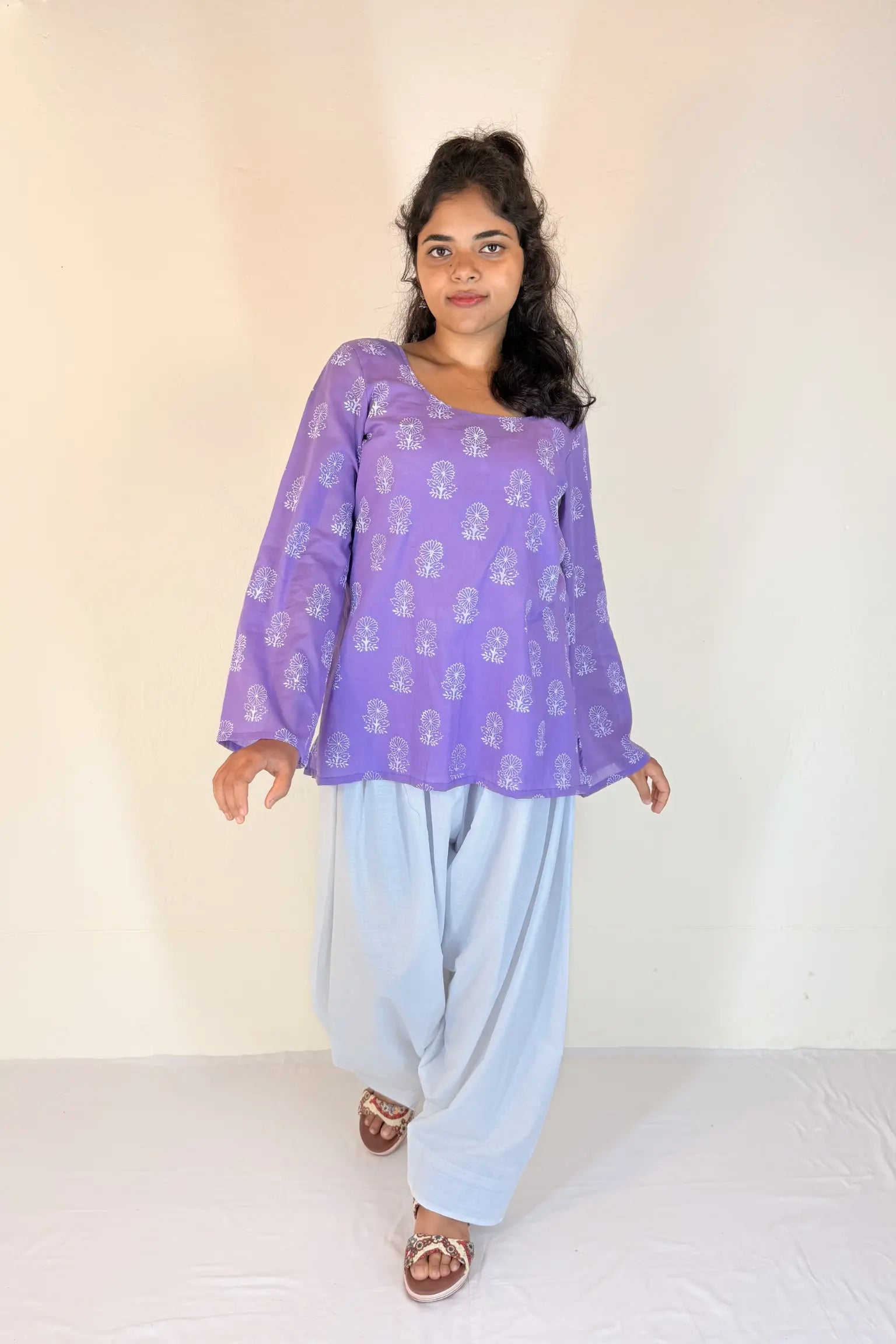 Woman wearing a purple top and light blue pants on a white background