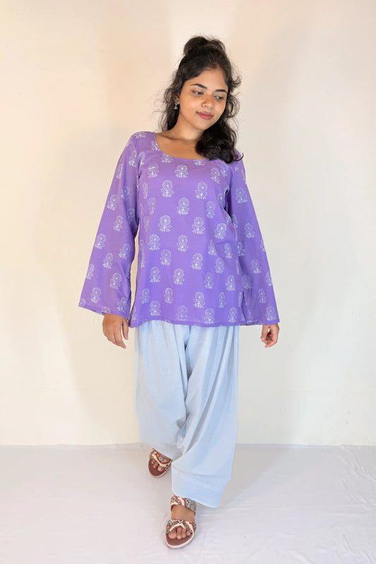 Woman wearing a purple top and light blue pants against a white background