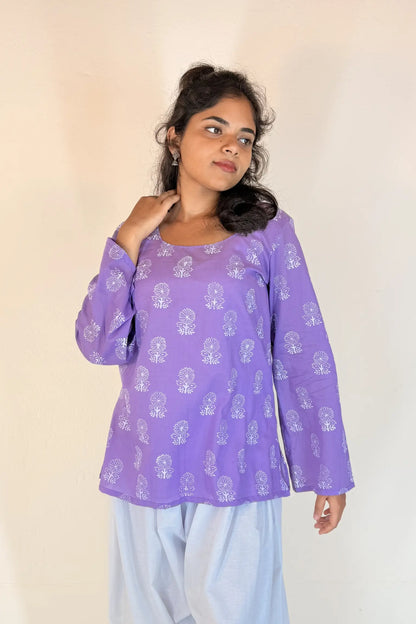 Woman wearing a purple patterned top with light blue pants against a plain background
