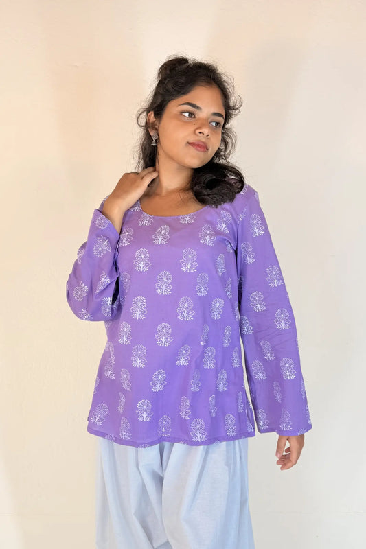 Woman wearing a purple patterned top with light blue pants against a plain background