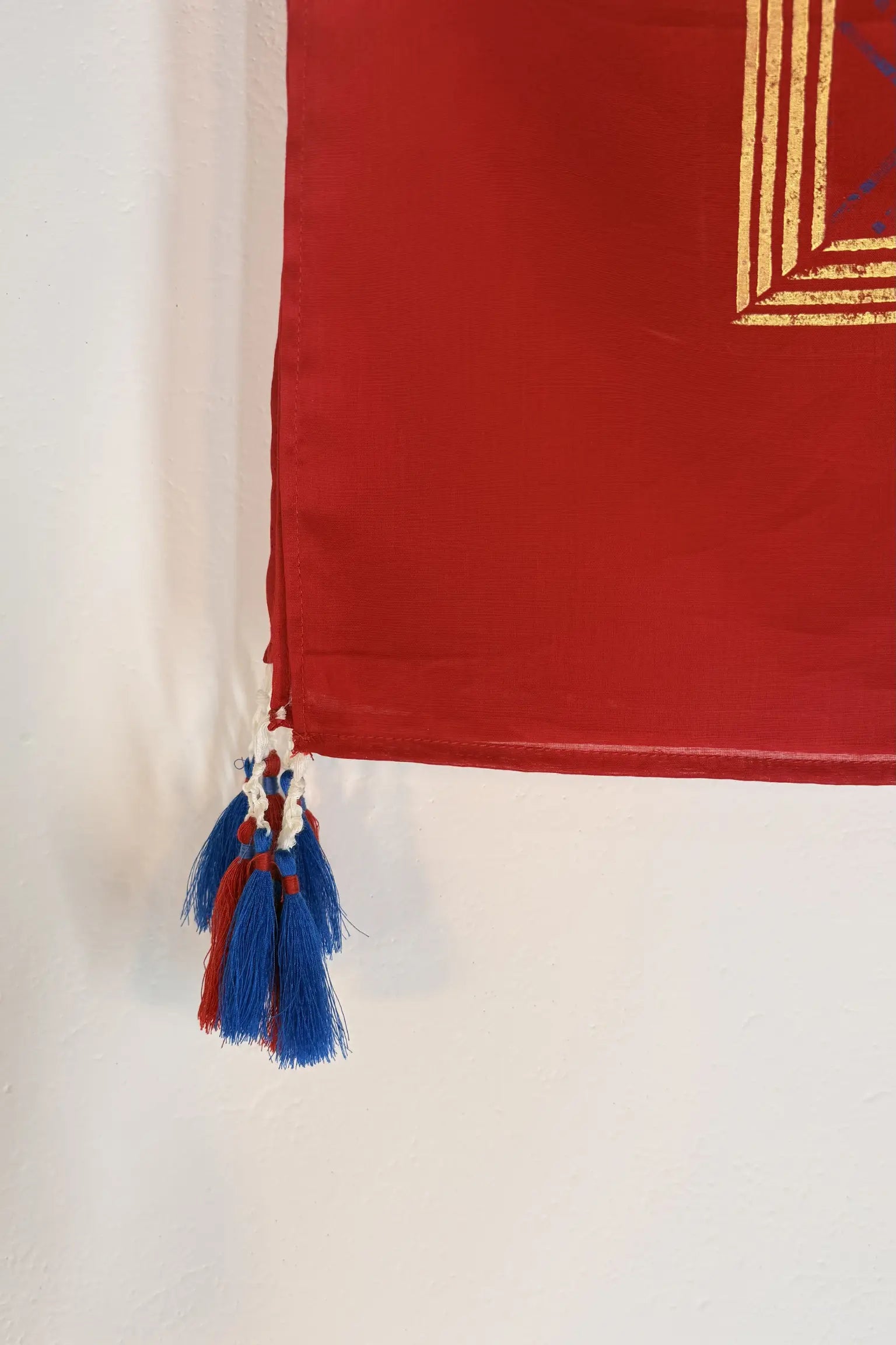 Red cotton scarf with gold geometric block print and handcrafted blue and red tassel detailing at the edge