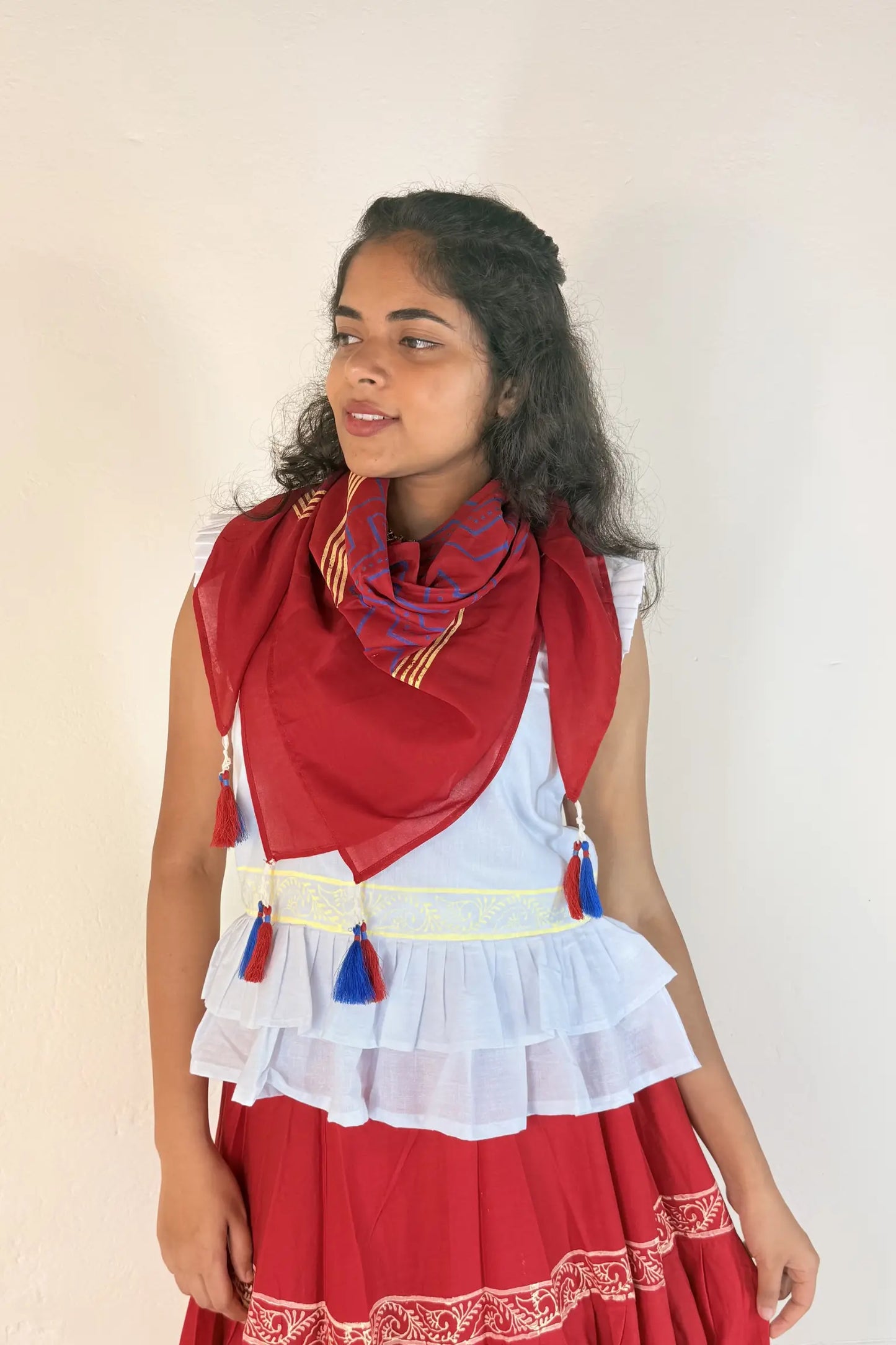 Woman wearing a red and white traditional outfit with a scarf on a plain background