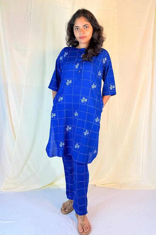 Woman wearing a blue checkered outfit with white patterns against a light curtain background