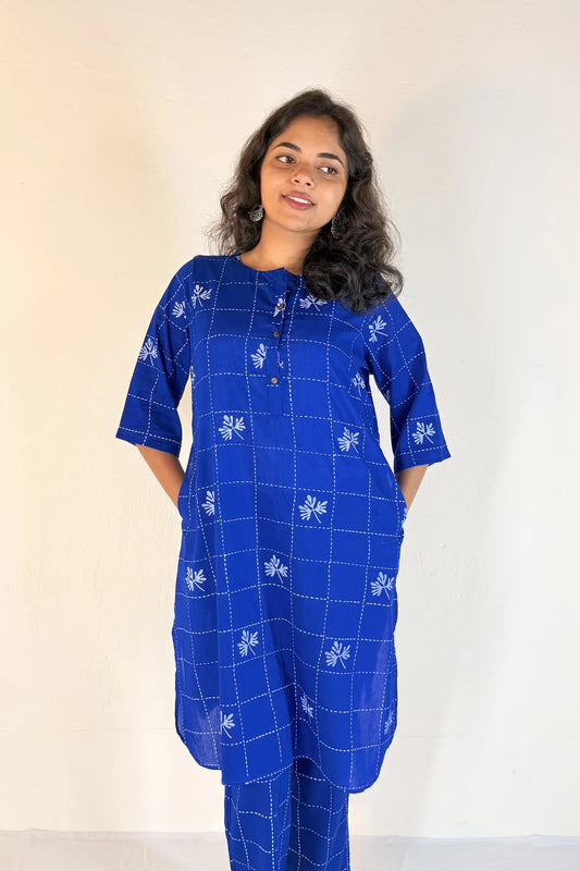 Woman wearing a blue traditional outfit with white patterns against a plain background