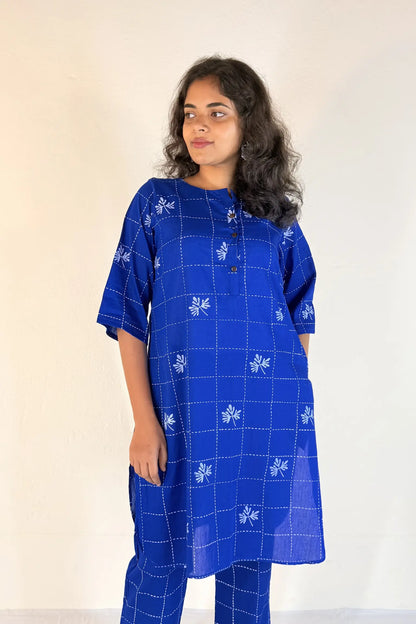 Woman wearing a blue checkered dress with white patterns on a plain background