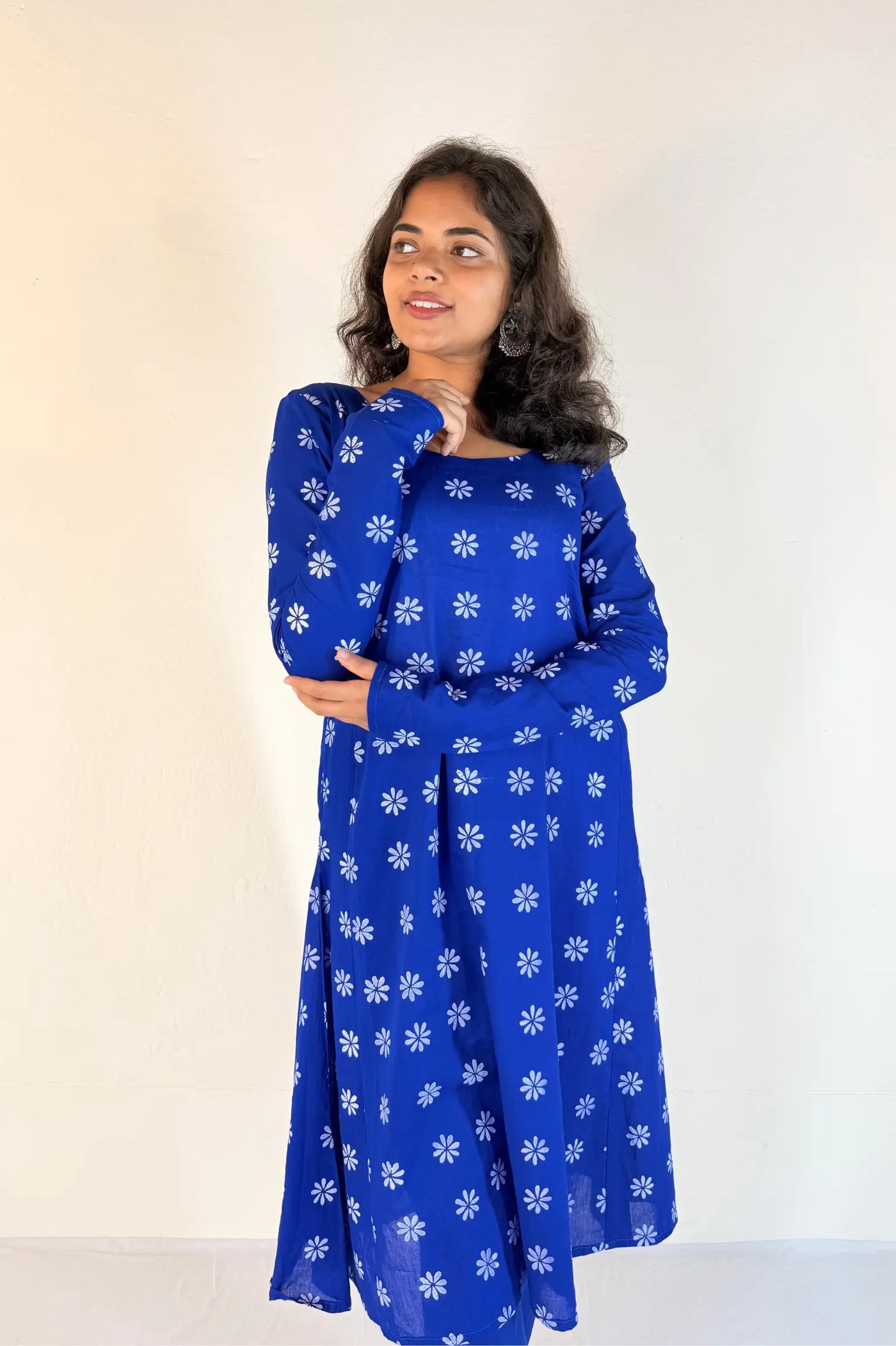 Woman wearing a blue dress with white floral patterns against a plain background