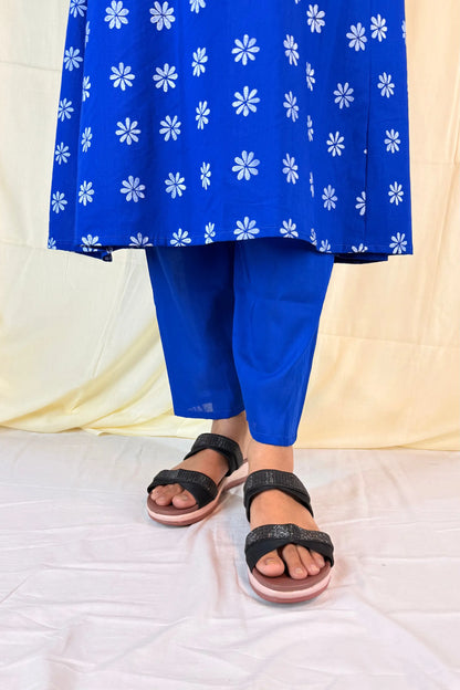 Person wearing a blue dress with white floral patterns and black sandals on a light background