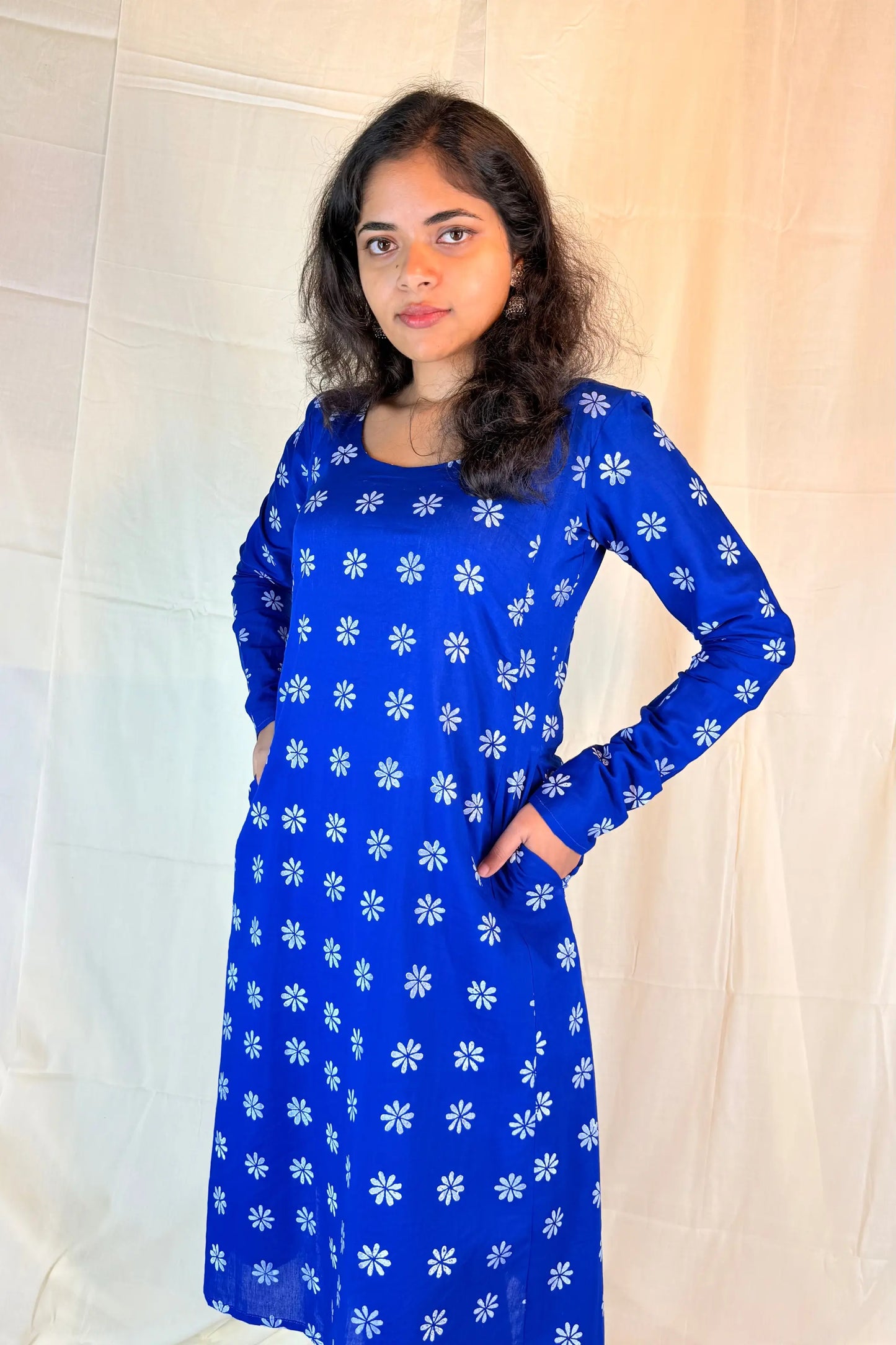 Woman wearing a blue dress with white floral patterns against a plain background