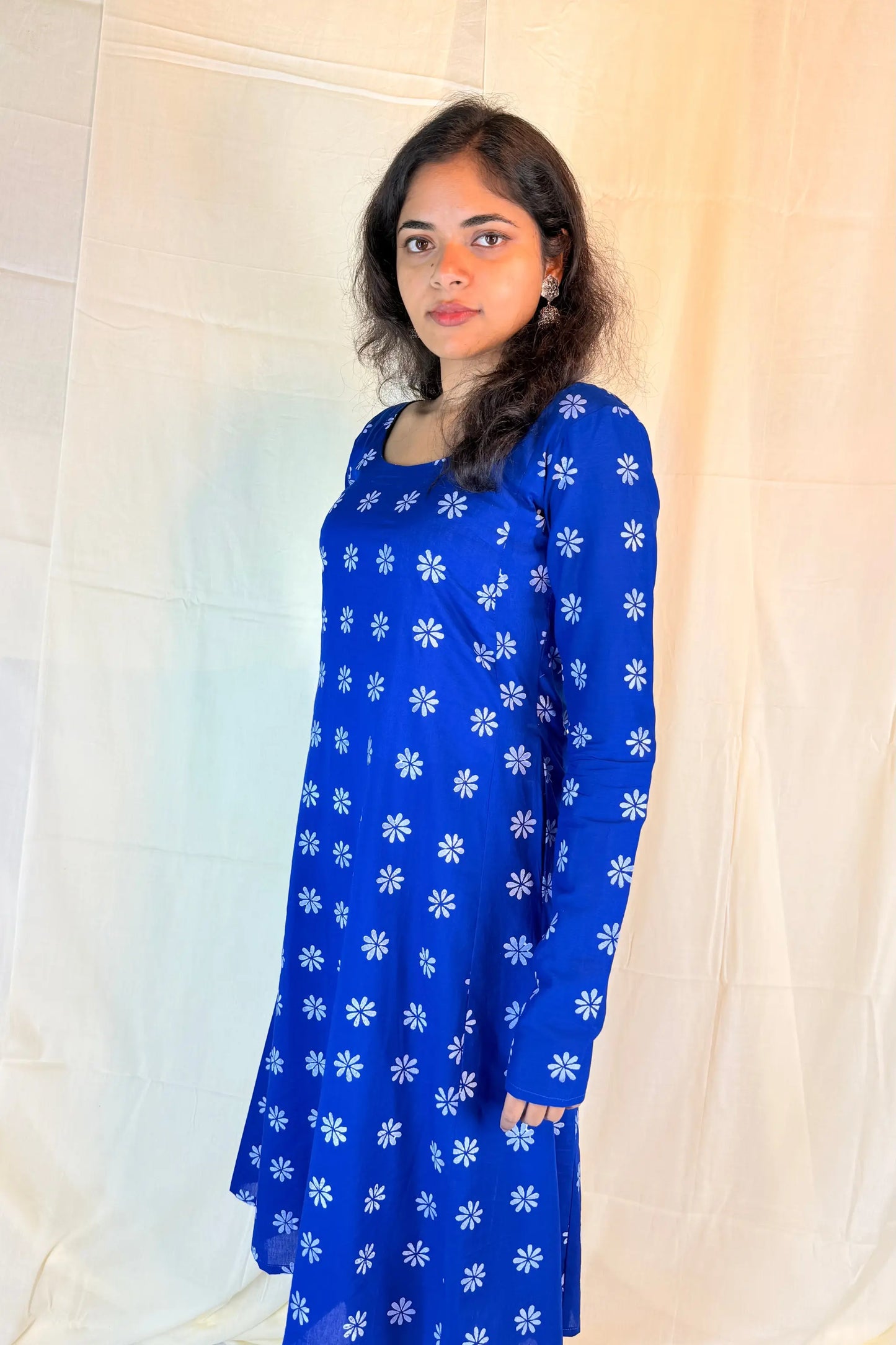 Woman wearing a blue dress with white floral patterns against a plain background