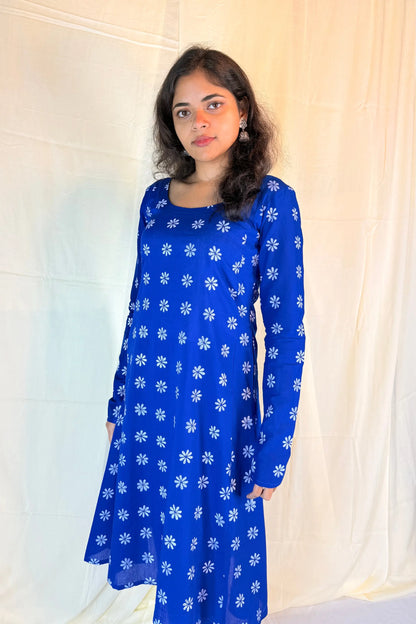 Woman wearing a blue dress with white floral patterns against a light background