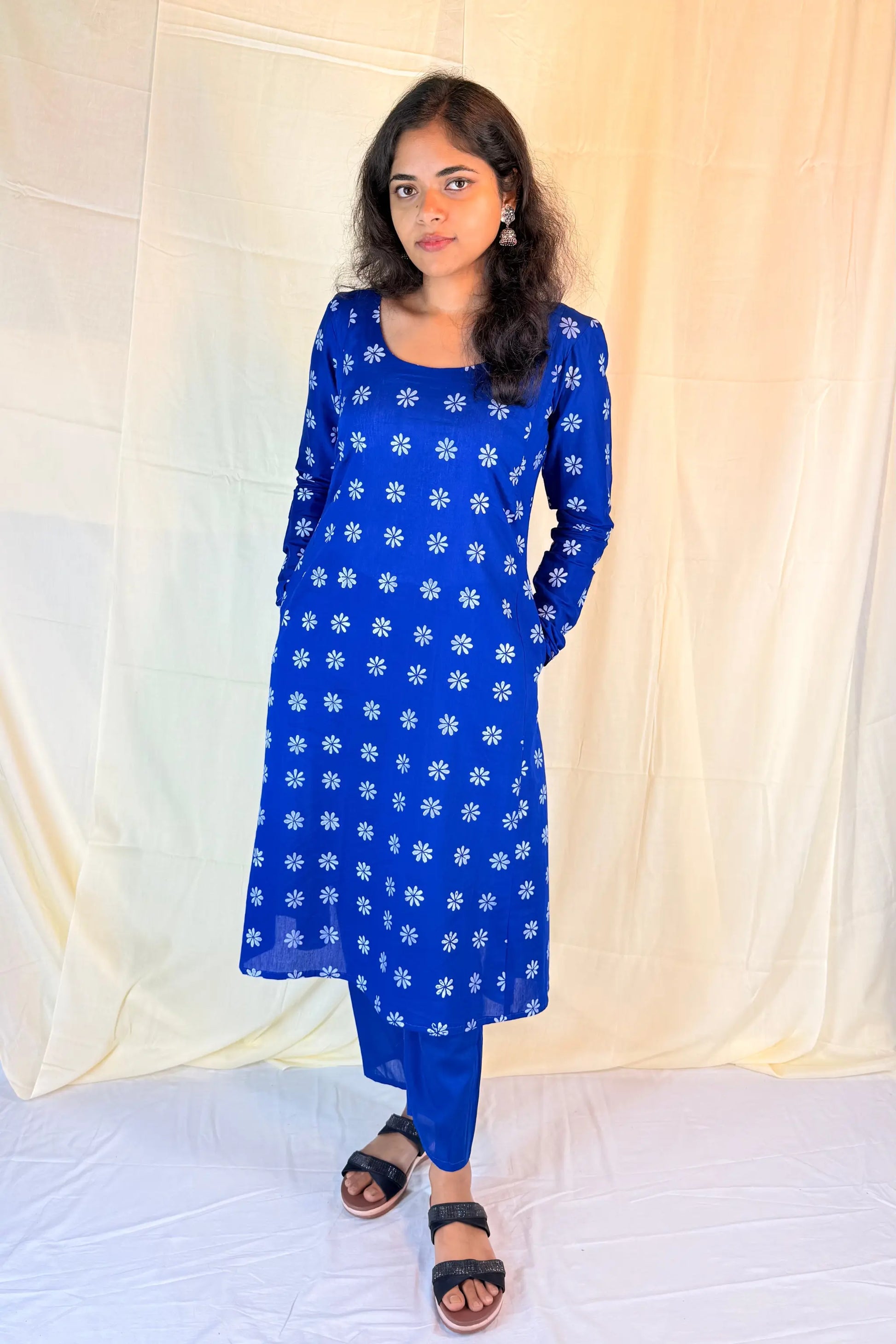 Woman wearing a blue kurta with white floral patterns against a light yellow curtain background